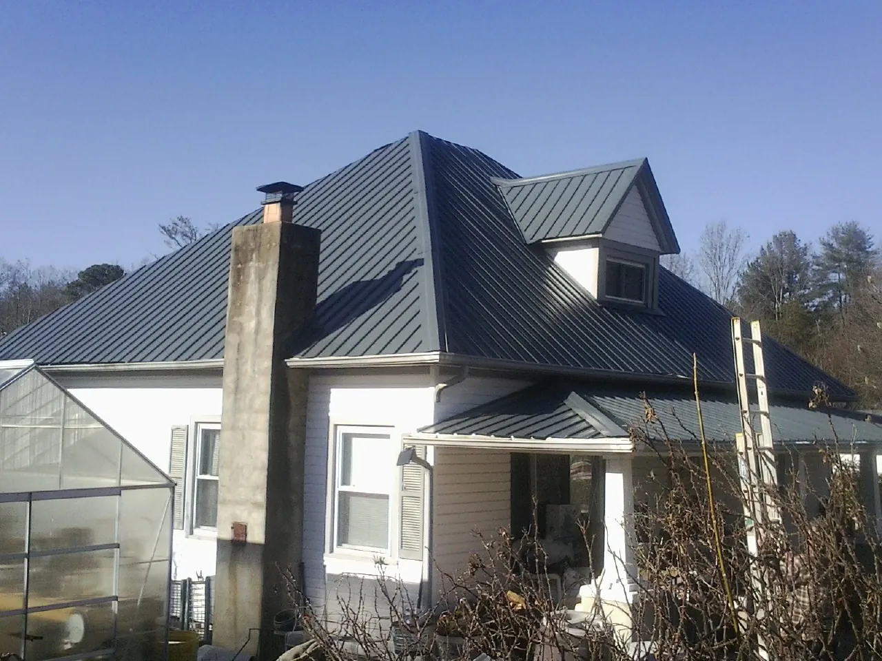 Dark blue standing seam metal roof on a white farmhouse with dormer — Slate & Tile Roof Repair by Roofing Brothers in Waverly