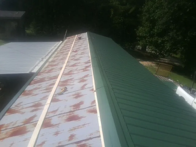 Old rusted panels beside newly installed green metal roofing — Wind Damage Roof Repair by Roofing Brothers in Waverly